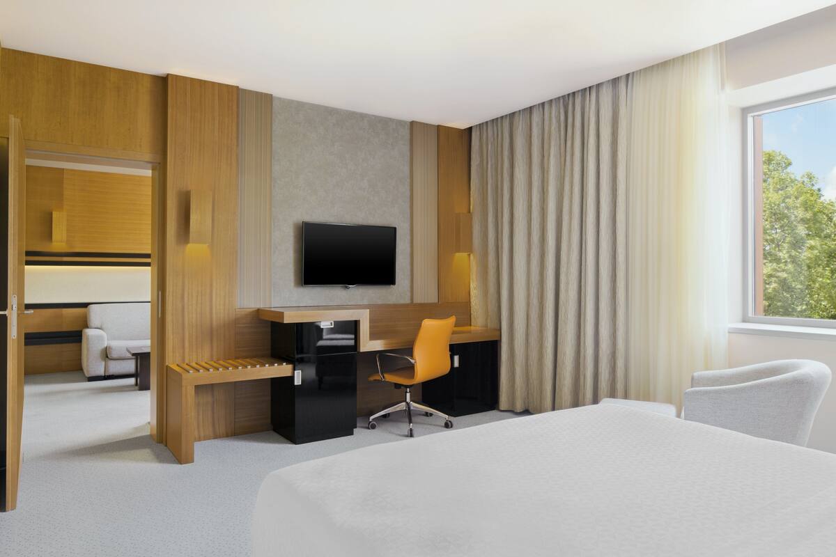 Une chambre d’hôtel avec un lit, un bureau, une chaise, une télévision et une fenêtre avec des rideaux.