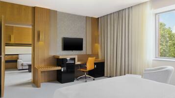Quarto de hotel com uma cama, uma escrivaninha, uma cadeira, uma televisão e uma janela com cortinas.