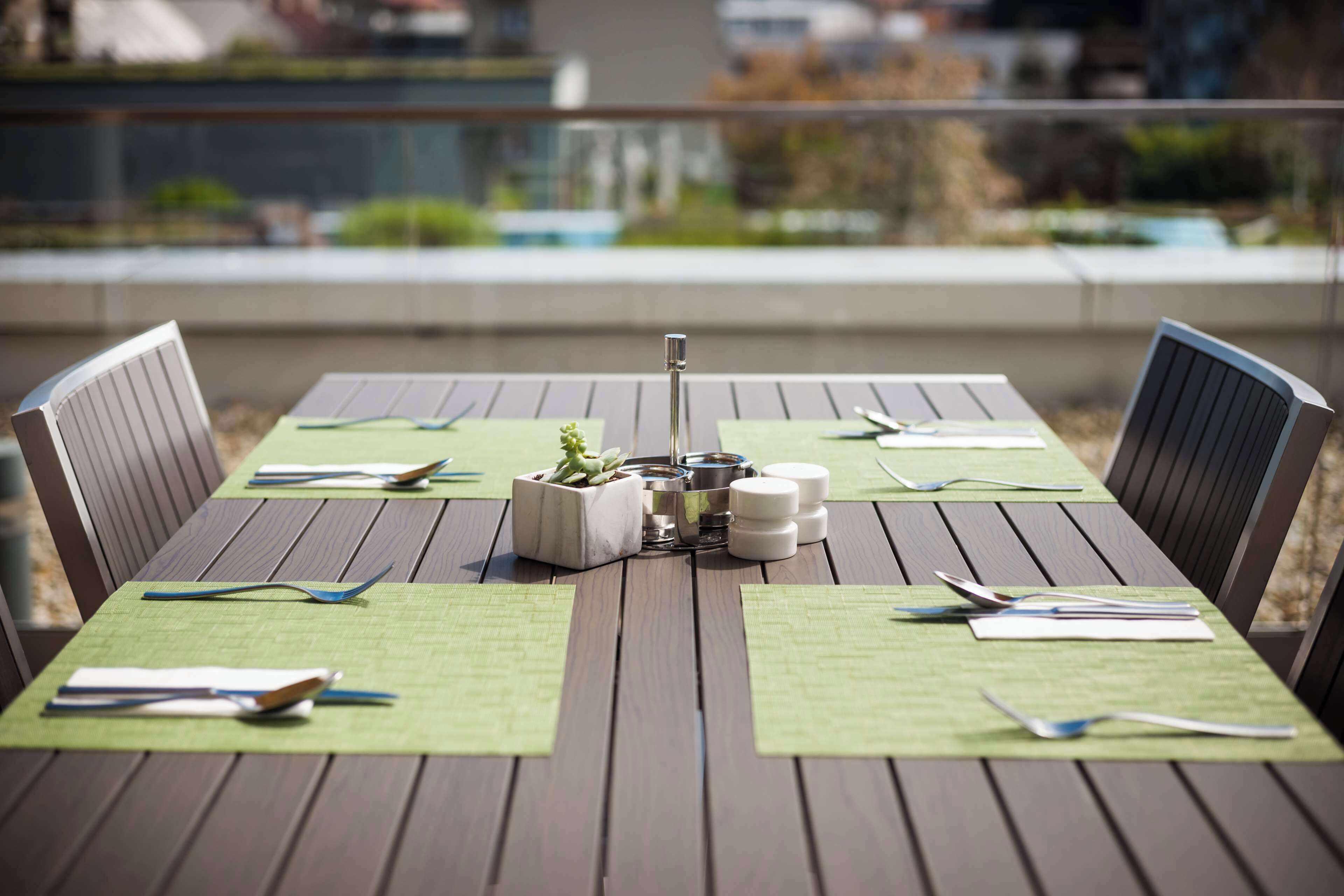A wooden dining table with green placemats, cutlery, and a centerpiece.