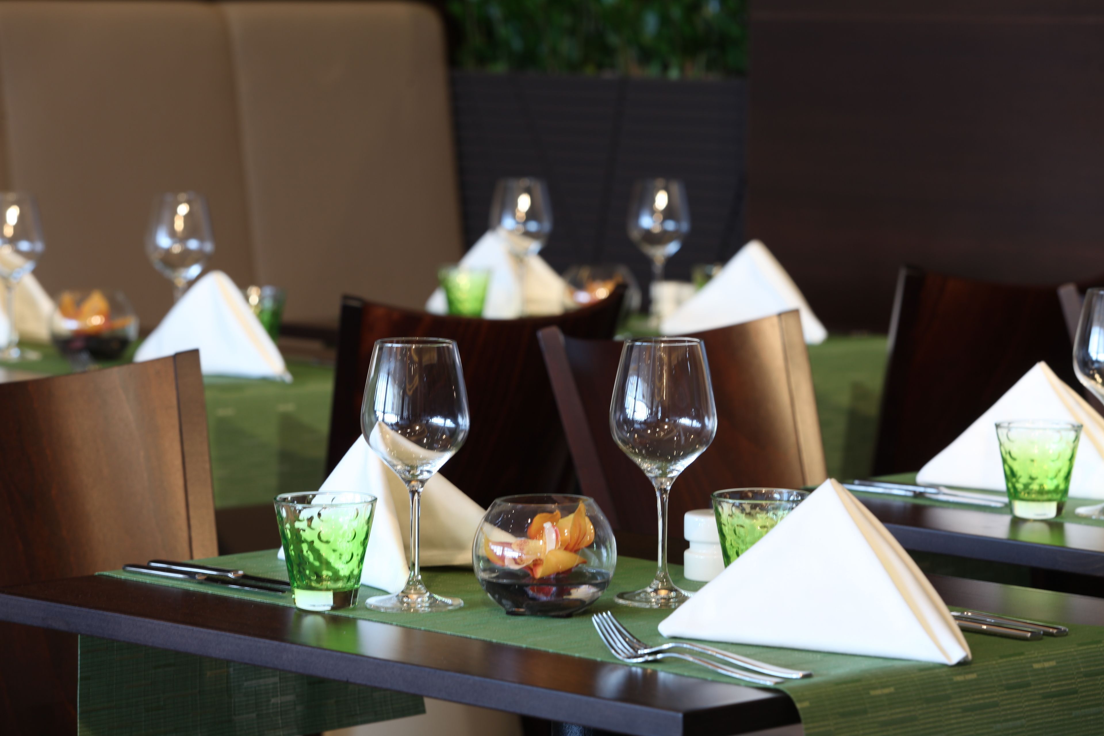 A dining table set with wine glasses, a green glass, a napkin, and cutlery.