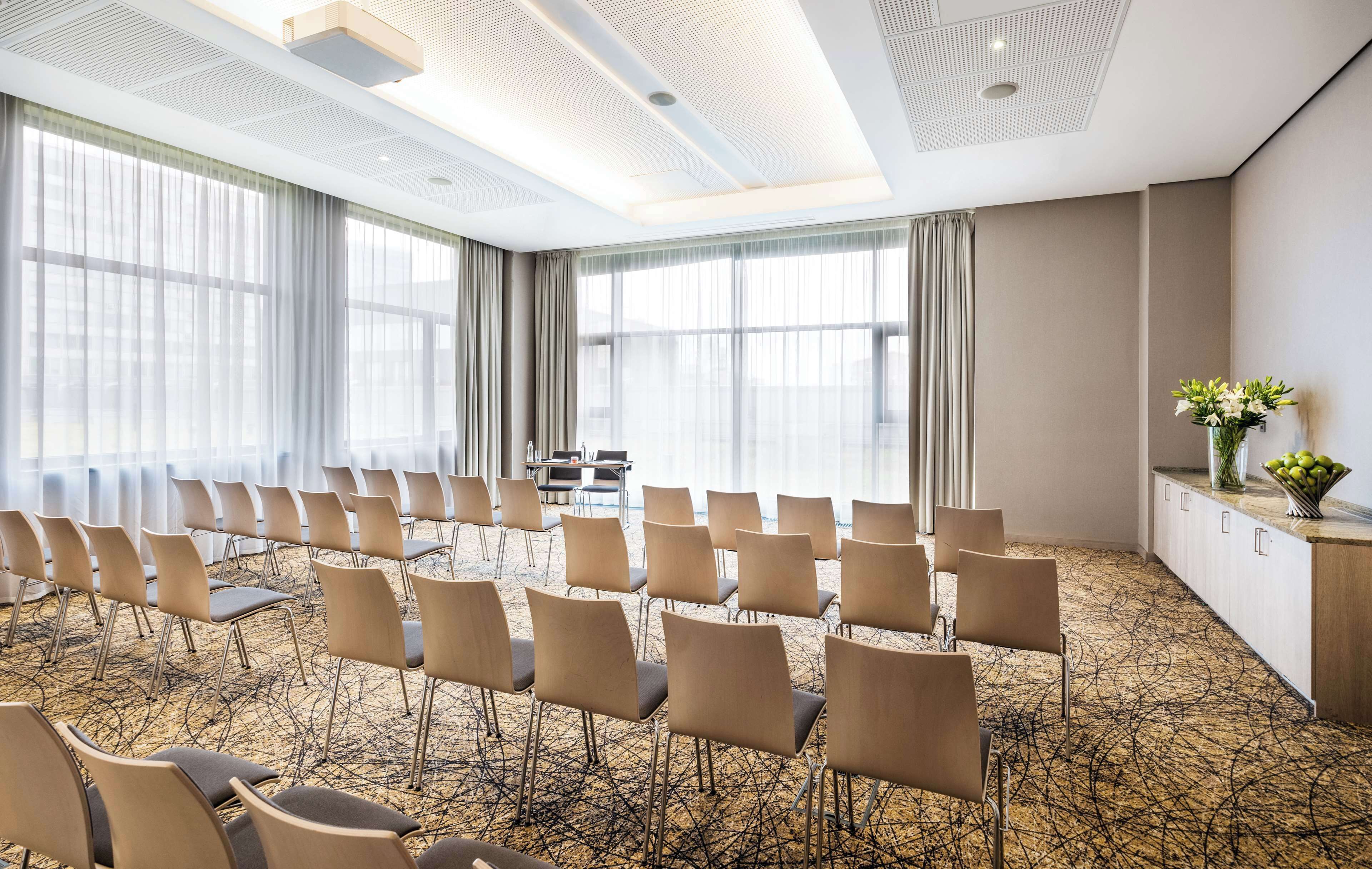 A conference room with rows of chairs, a long table, and large windows.