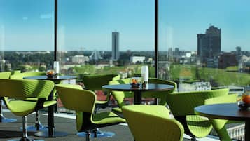 A modern indoor seating area with green chairs and tables, large windows offering a city view.