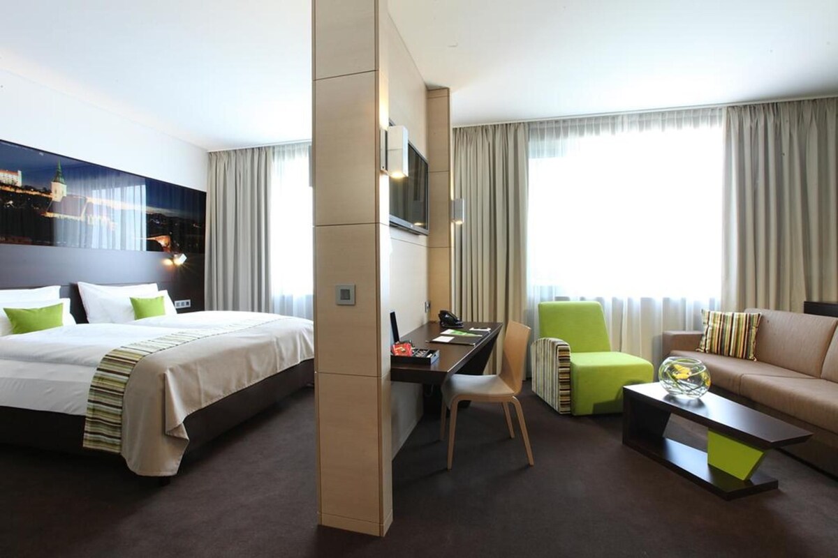 Habitació d'hotel amb llit, escriptori, cadira, sofà i televisió.