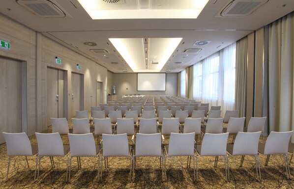 A conference room with rows of white chairs, a large screen, and a carpeted floor.