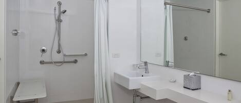 Un baño moderno con cabina de ducha de vidrio, un lavabo blanco, un espejo y una pequeña mesita de tocador.