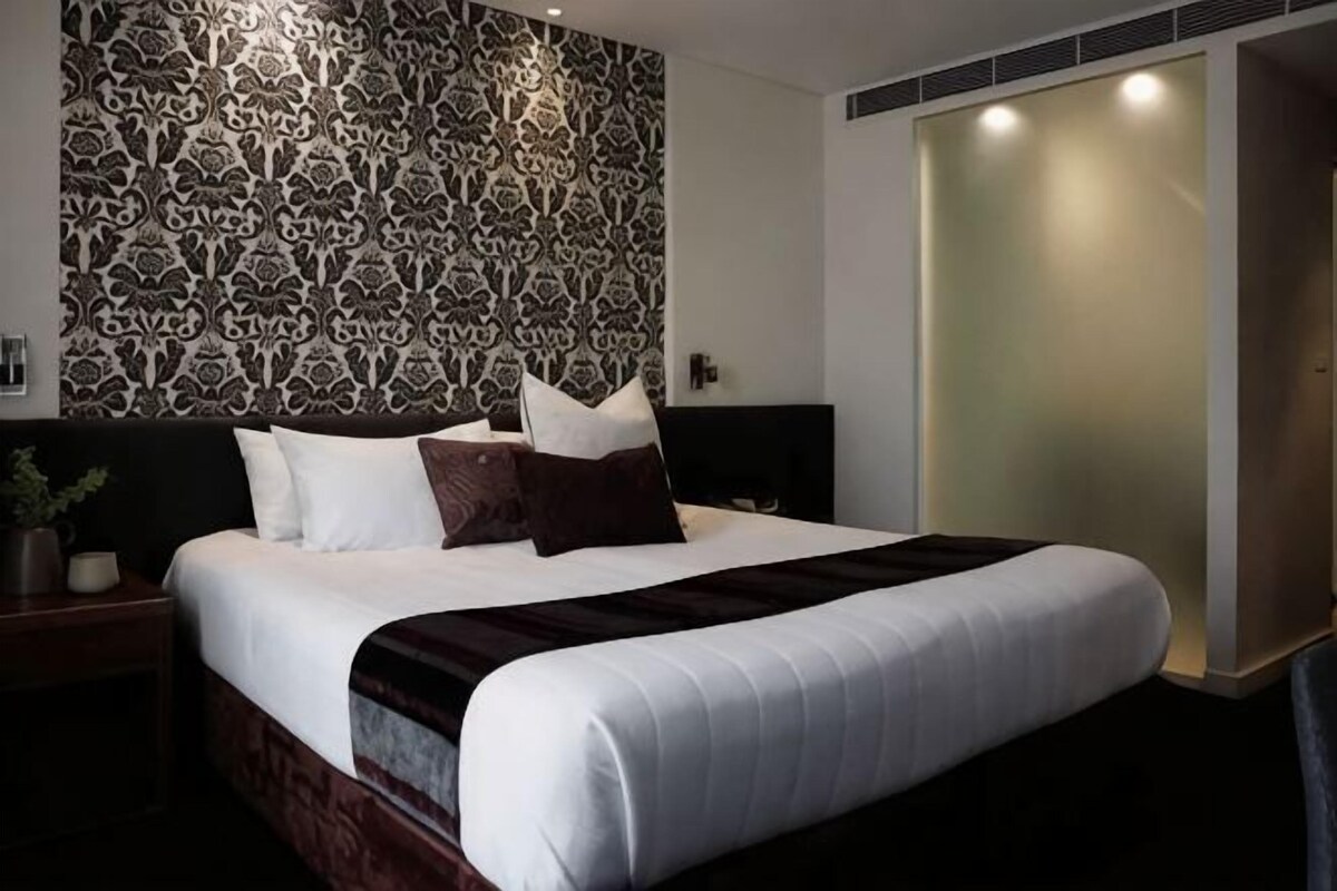 A modern hotel room with a large bed, a patterned wall, and a sliding door.