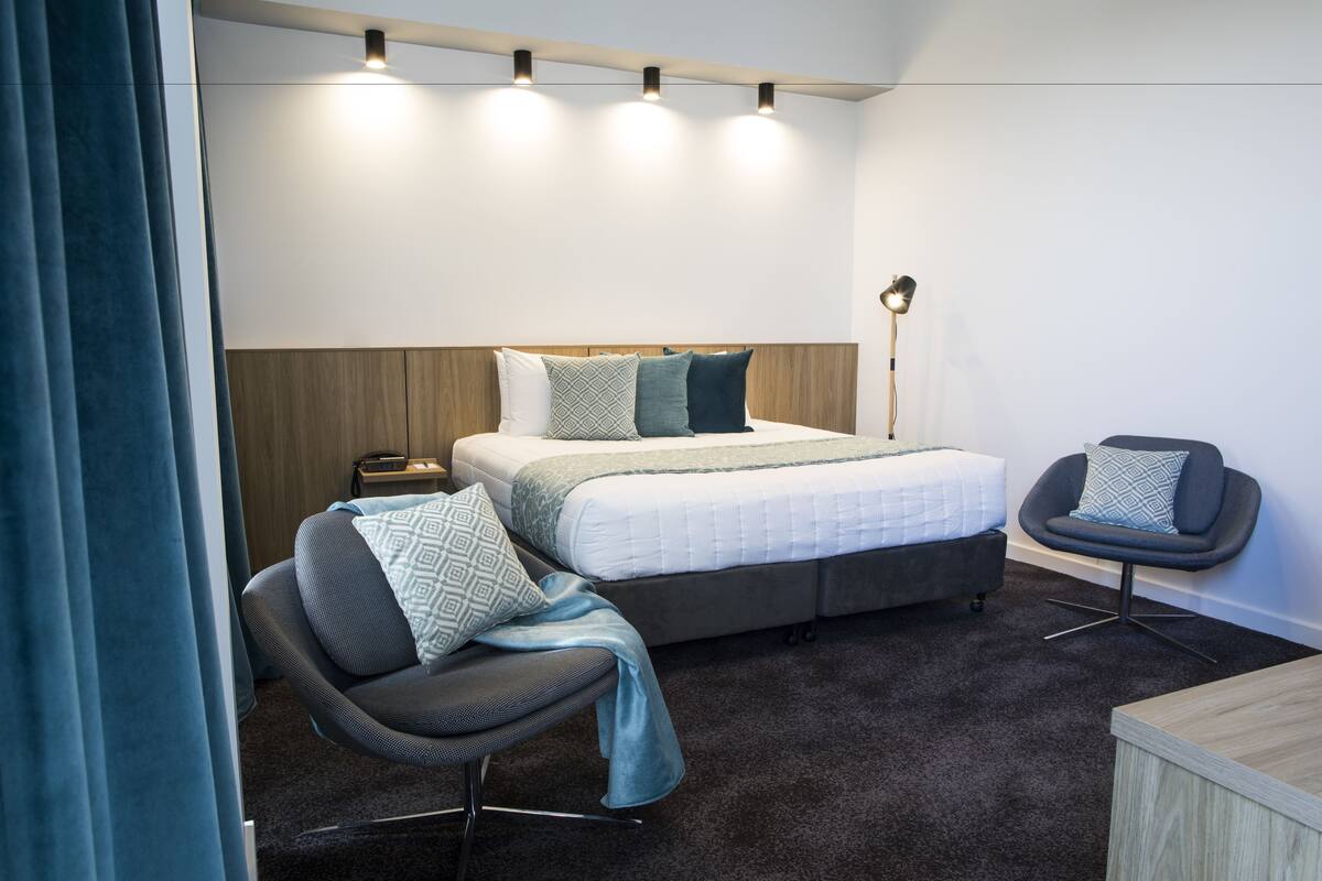 Una habitación de hotel moderna con una cama, una silla, un escritorio y una lámpara.