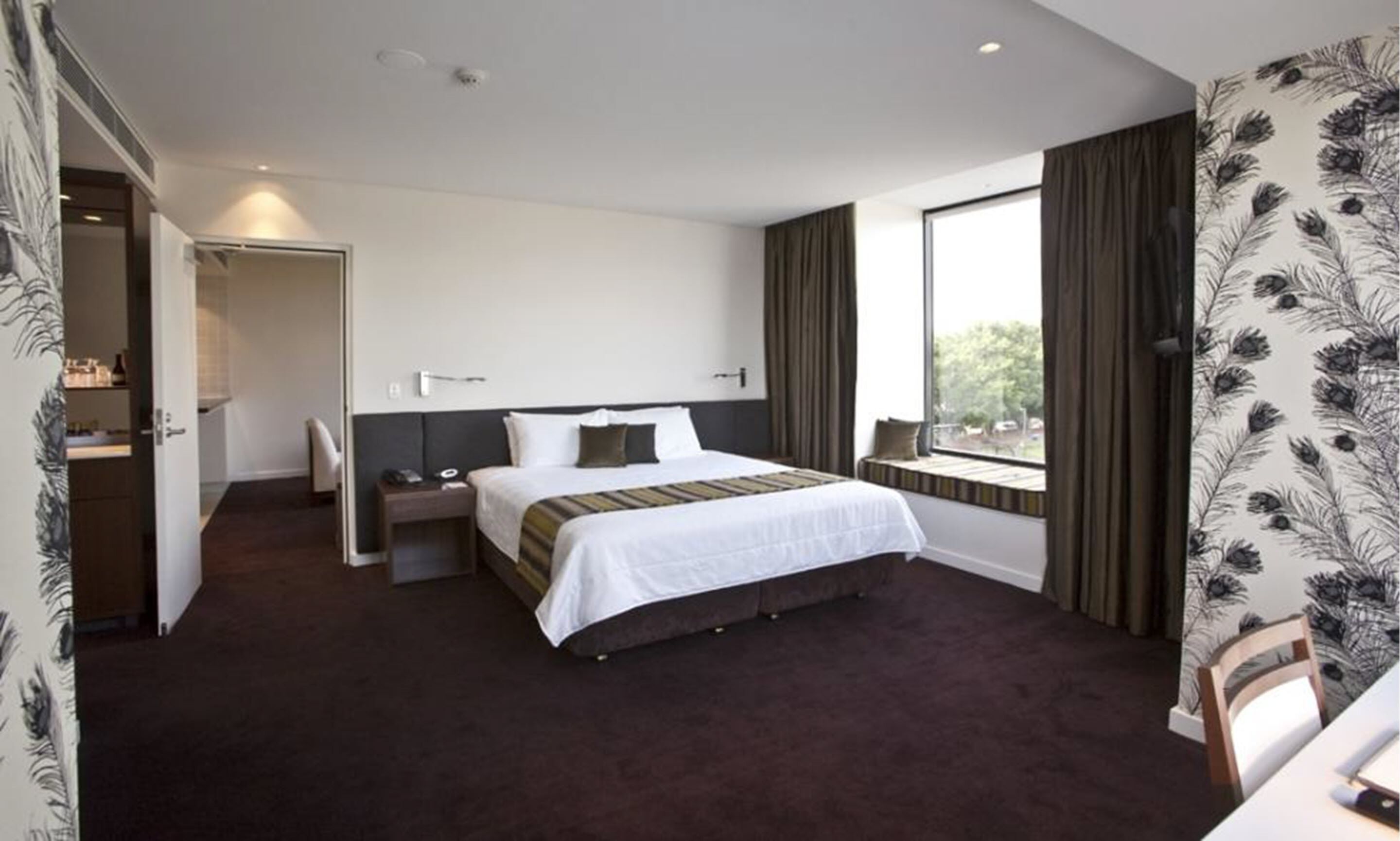 A hotel room with a large bed, a bedside table, a window with curtains, and a view of the outdoors.