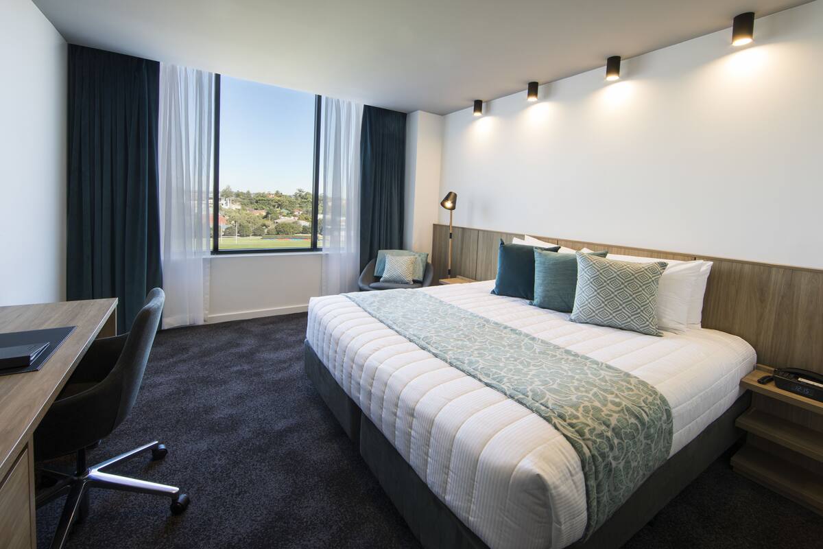 Habitación de hotel con una cama grande, un escritorio, una silla y vistas al exterior.