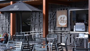 An outdoor seating area with metal chairs and tables, a black umbrella, and a wooden sign with the word "BE" partially visible.