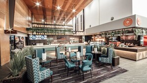 A modern restaurant with a bar area, seating with patterned chairs, and a wooden ceiling.