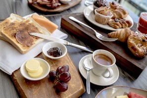 A breakfast setting with toast, butter, jam, grapes, croissants, muffins, and coffee on a wooden table.