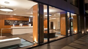 A modern hotel lobby with a reception desk, seating area, and a large glass wall.