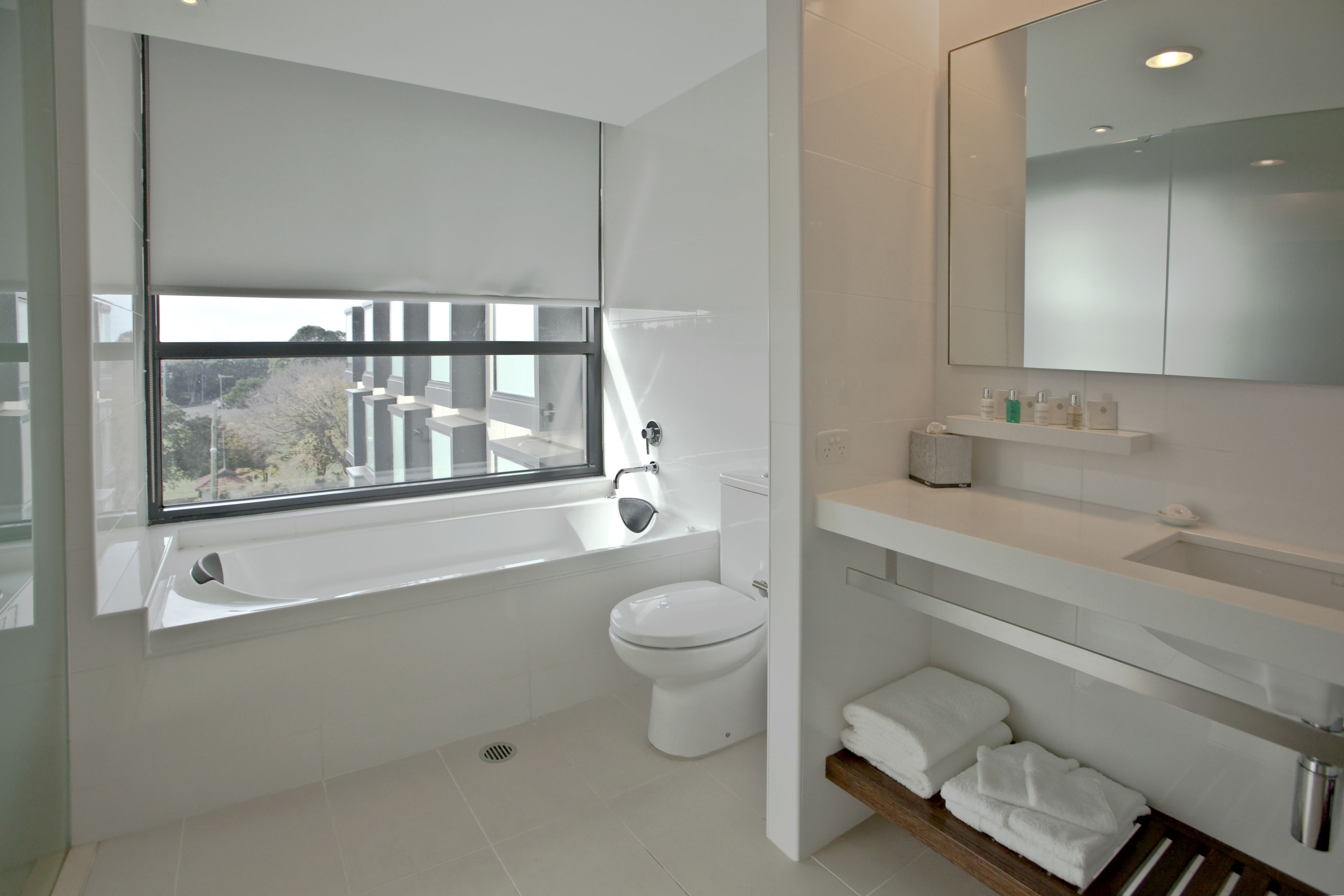A modern bathroom with a large window, a toilet, a sink, and a mirror.