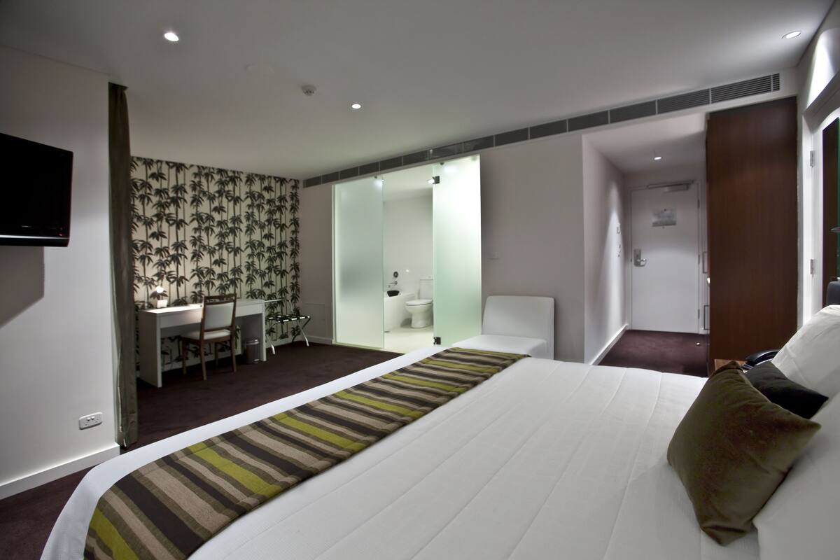 Habitación de hotel con cama, escritorio y baño a la vista tras una puerta abierta.