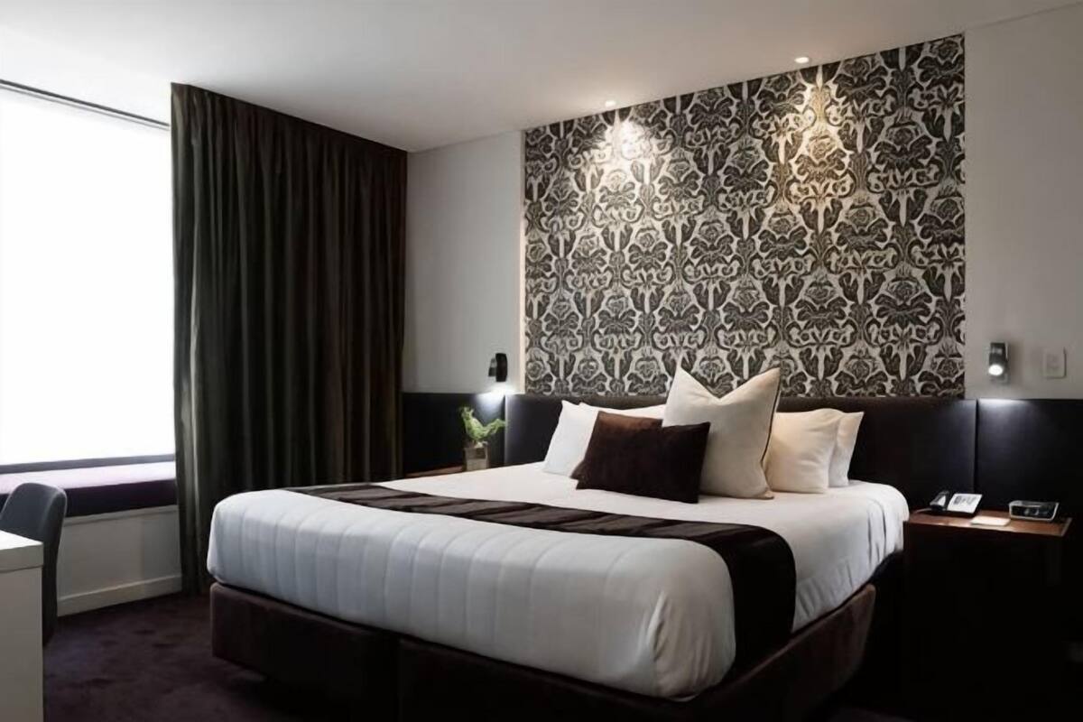 Una habitación de hotel con una cama grande, un escritorio, una mesita de noche y un papel tapiz estampado.