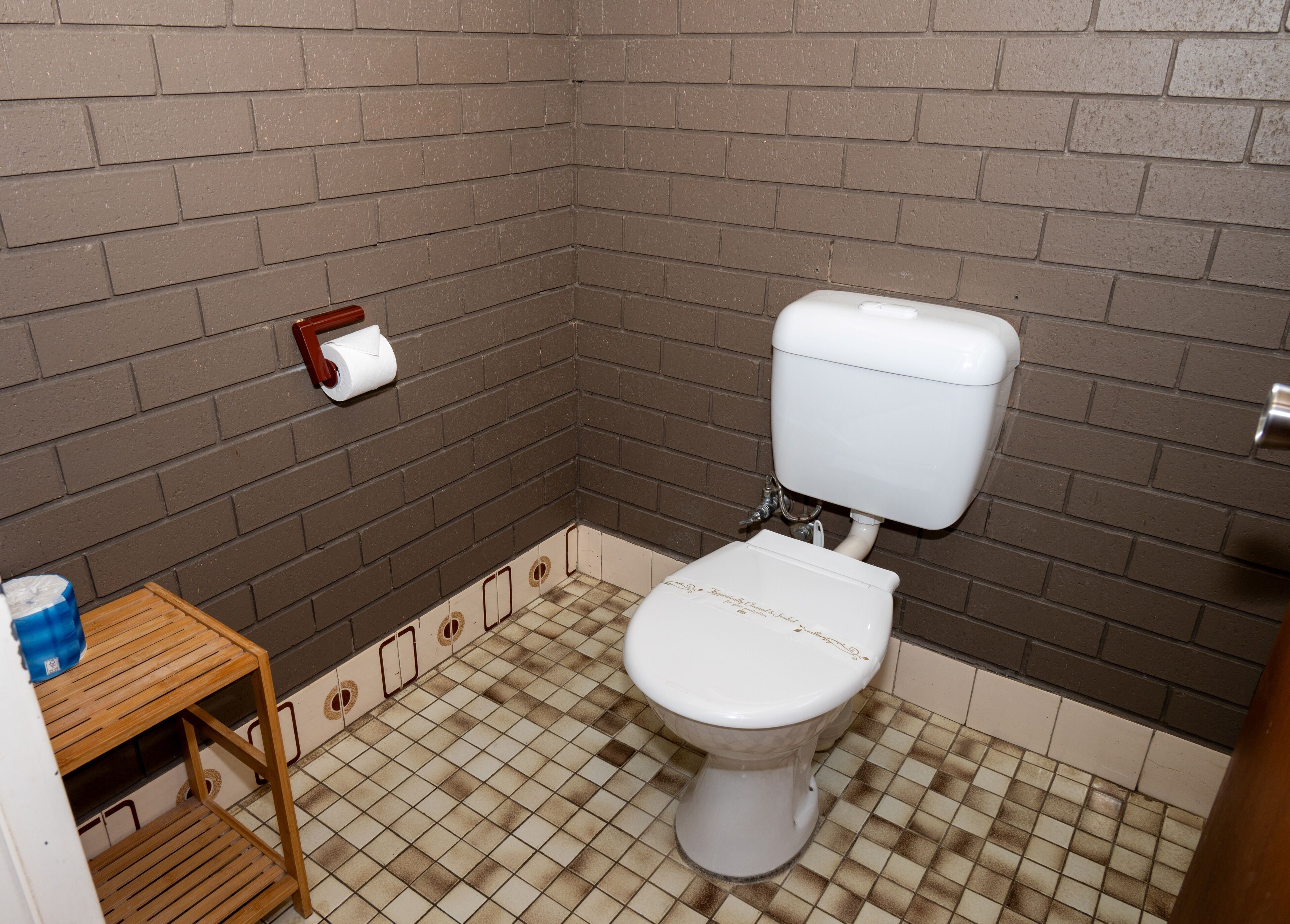 Une petite salle de bain avec des toilettes, une étagère en bois et un porte-rouleau de papier toilette fixé au mur.