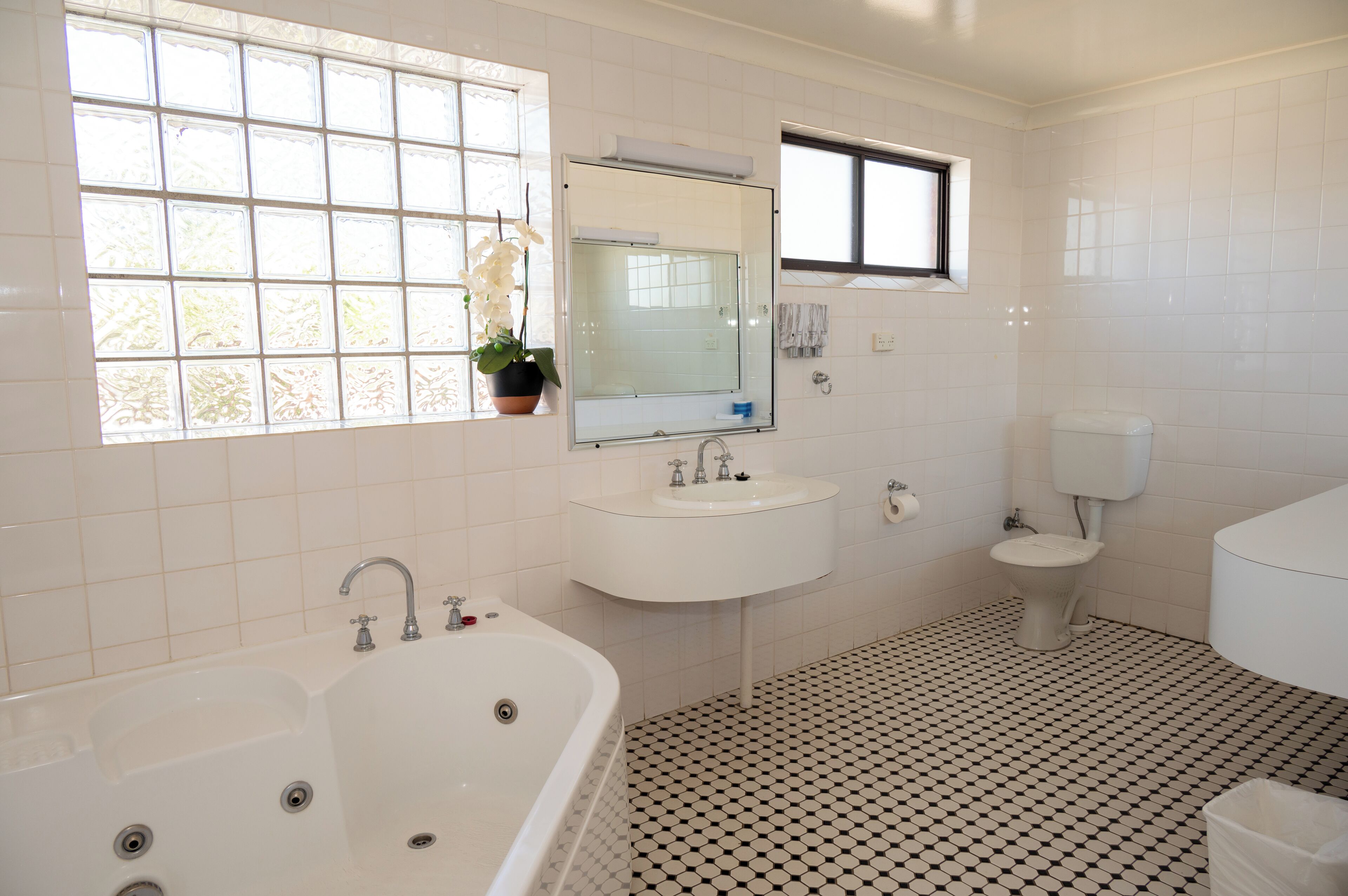 A bathroom with a bathtub, sink, toilet, and a window with a potted plant.