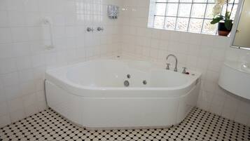 A bathroom with a large bathtub, a sink, and a window with a potted plant.