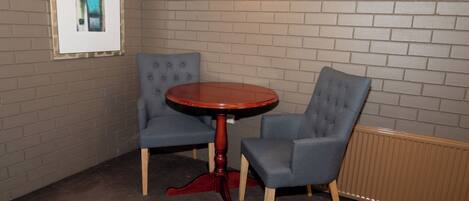 A room with a brick wall, a framed picture, a round wooden table, and two upholstered chairs.