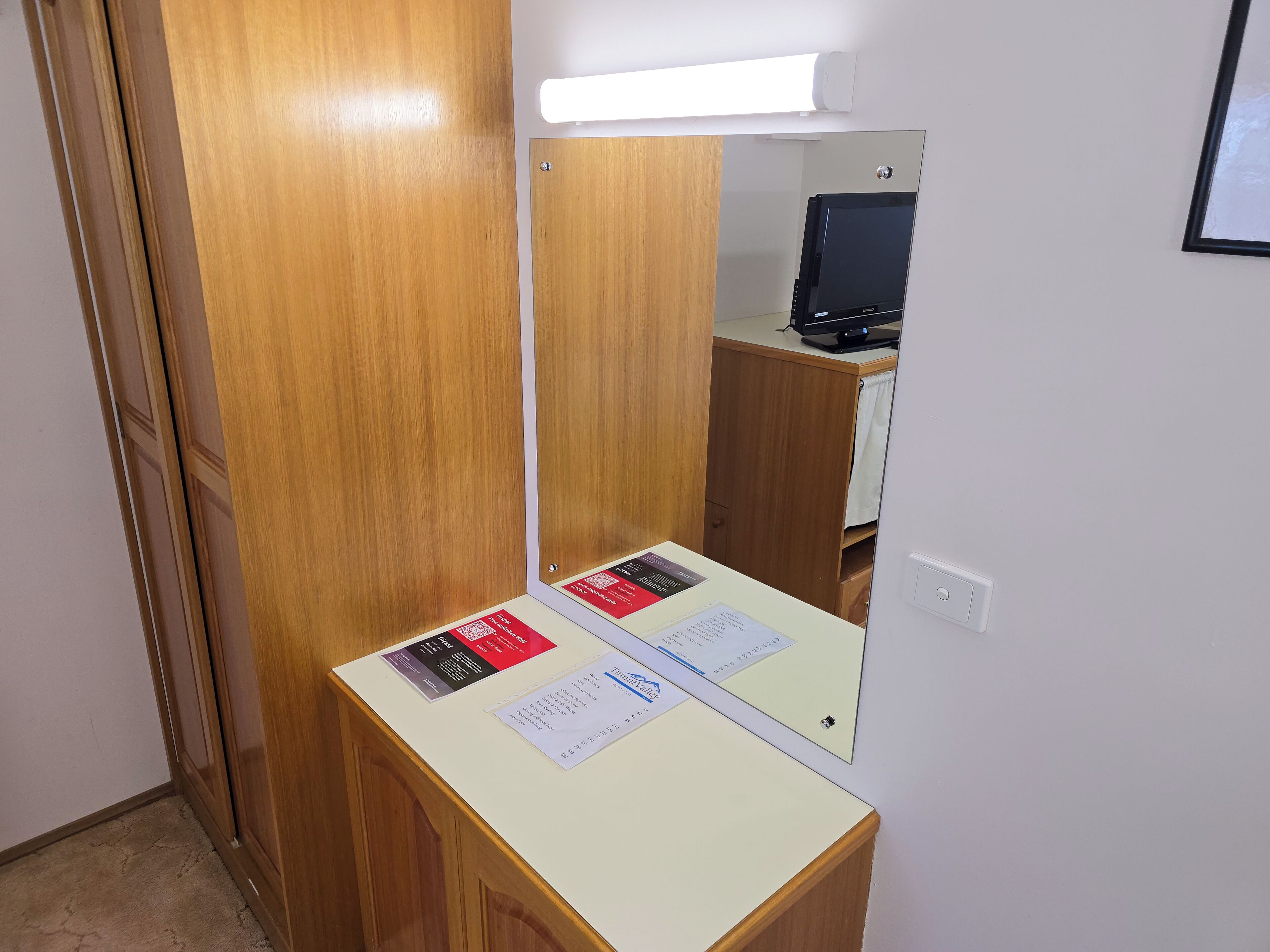 A room with a wooden wardrobe, a mirror, a desk with papers, and a computer monitor.