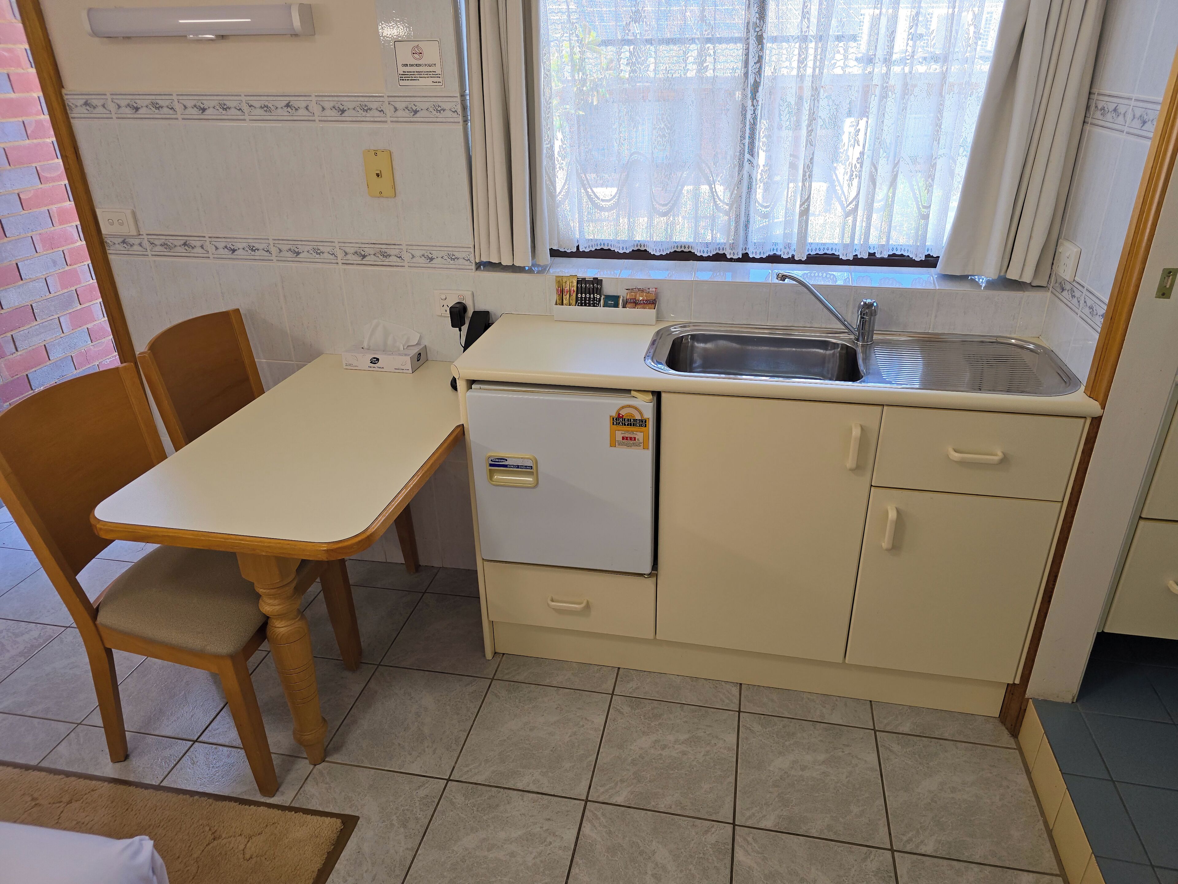 Et kompakt køkken med vask, lille køleskab og spiseplads med bord og stole.
