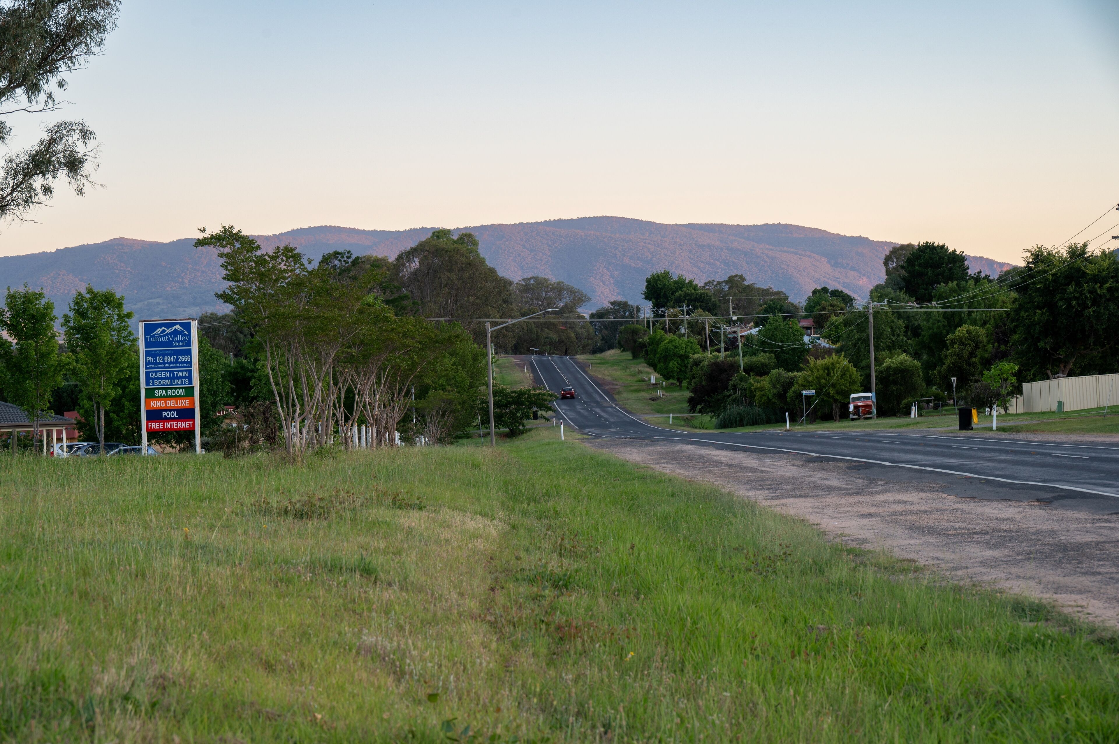 A road with a signboard listing amenities like 2 BDRM units, SPA room, KING DELUXE pool, and FREE internet.