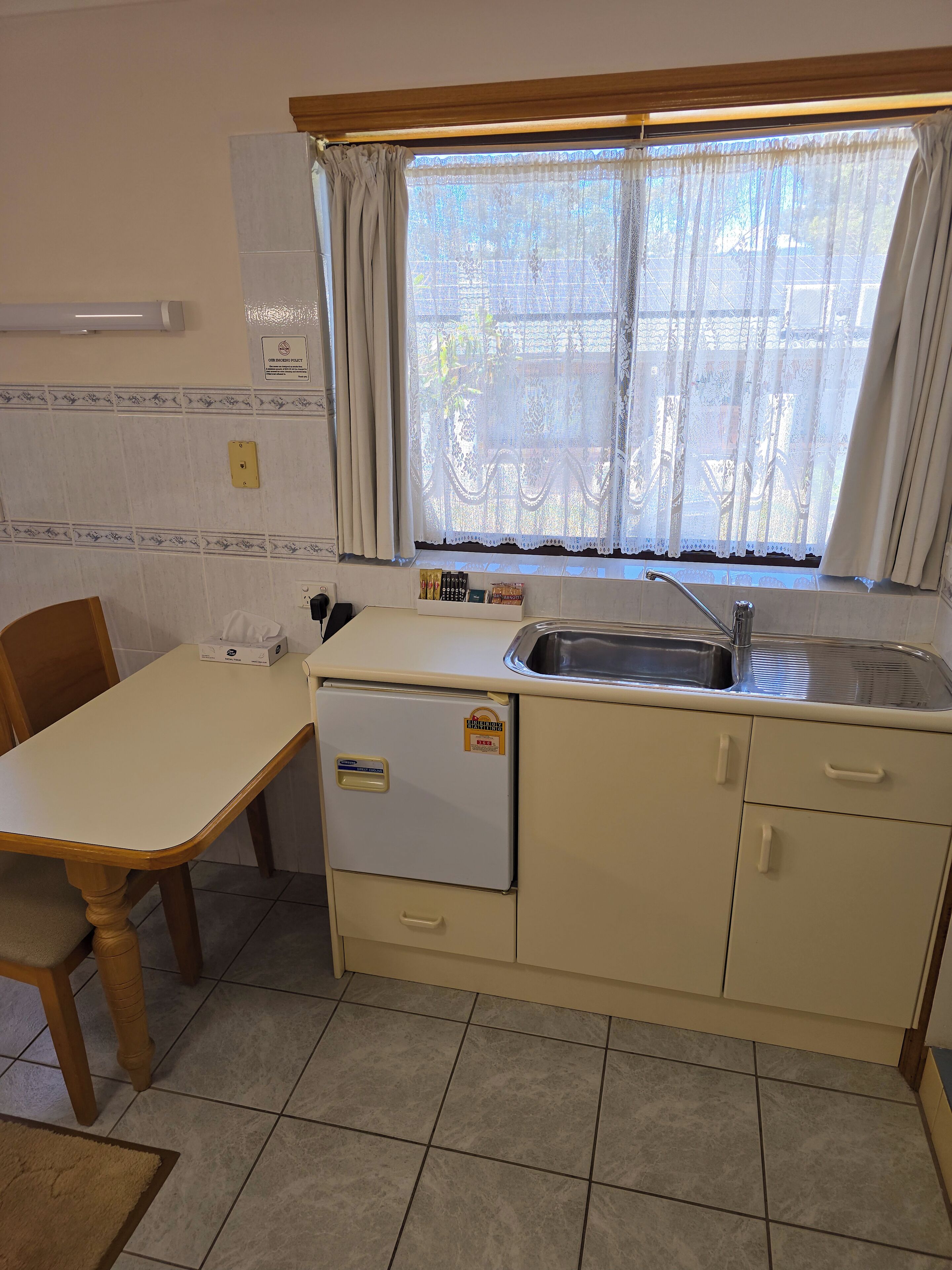 Una cocina compacta con un lavamanos, un refrigerador pequeño y una ventana con cortinas.