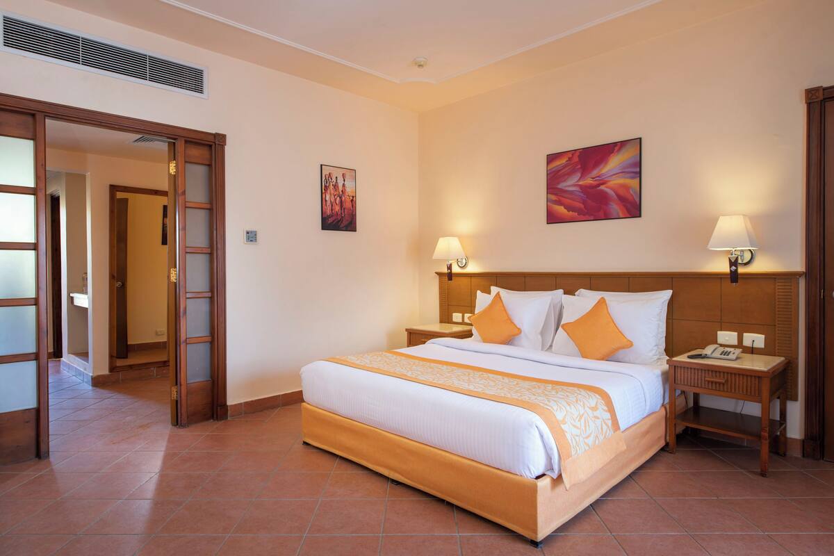 A hotel room with a large bed, two bedside tables, a nightstand, and a door leading to another room.
