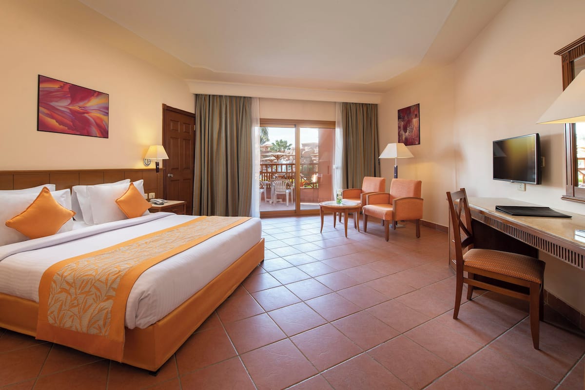 A hotel room with a bed, a desk, a chair, a television, and a balcony with a view.