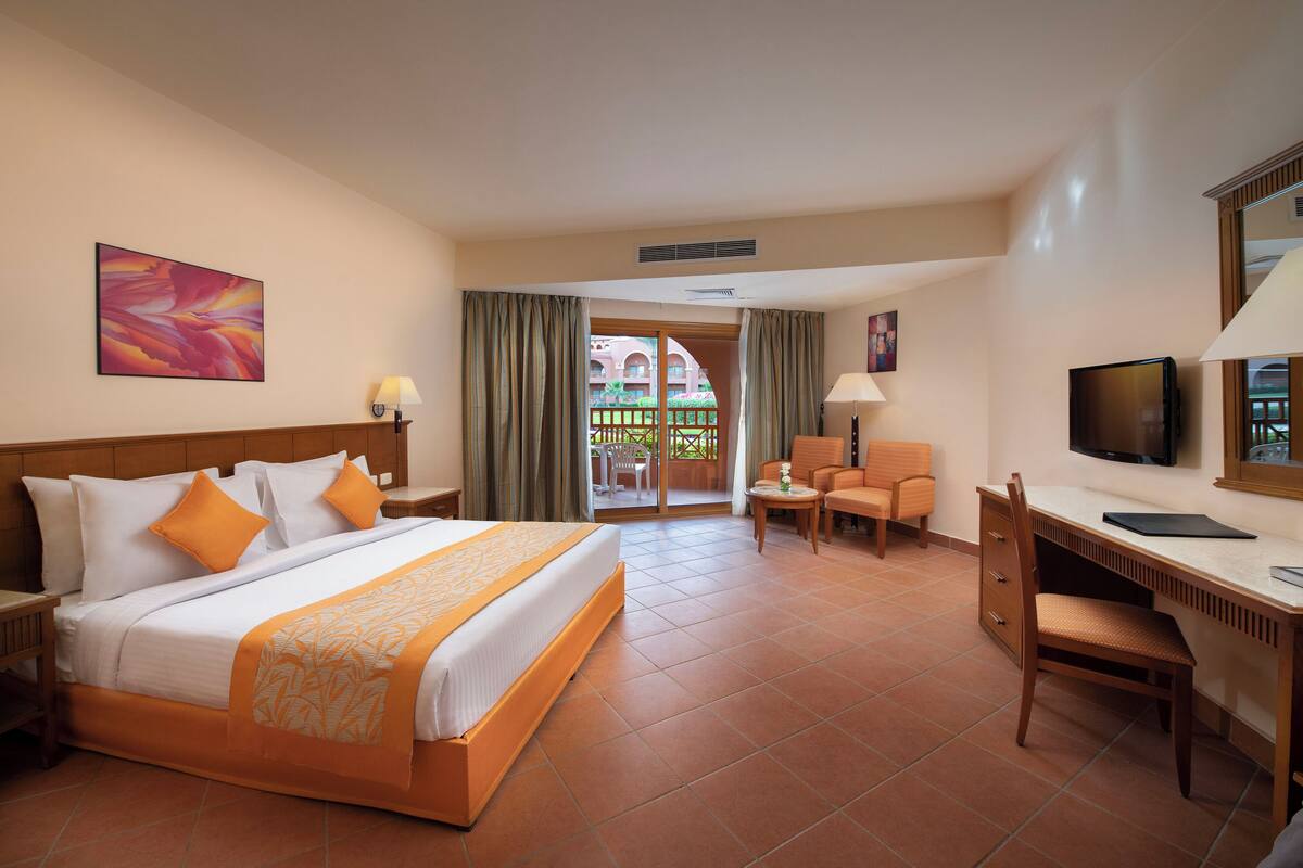 A hotel room with a bed, desk, chair, TV, and a balcony with a view.