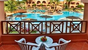 A balcony with a view of a swimming pool, palm trees, and a building with arches.