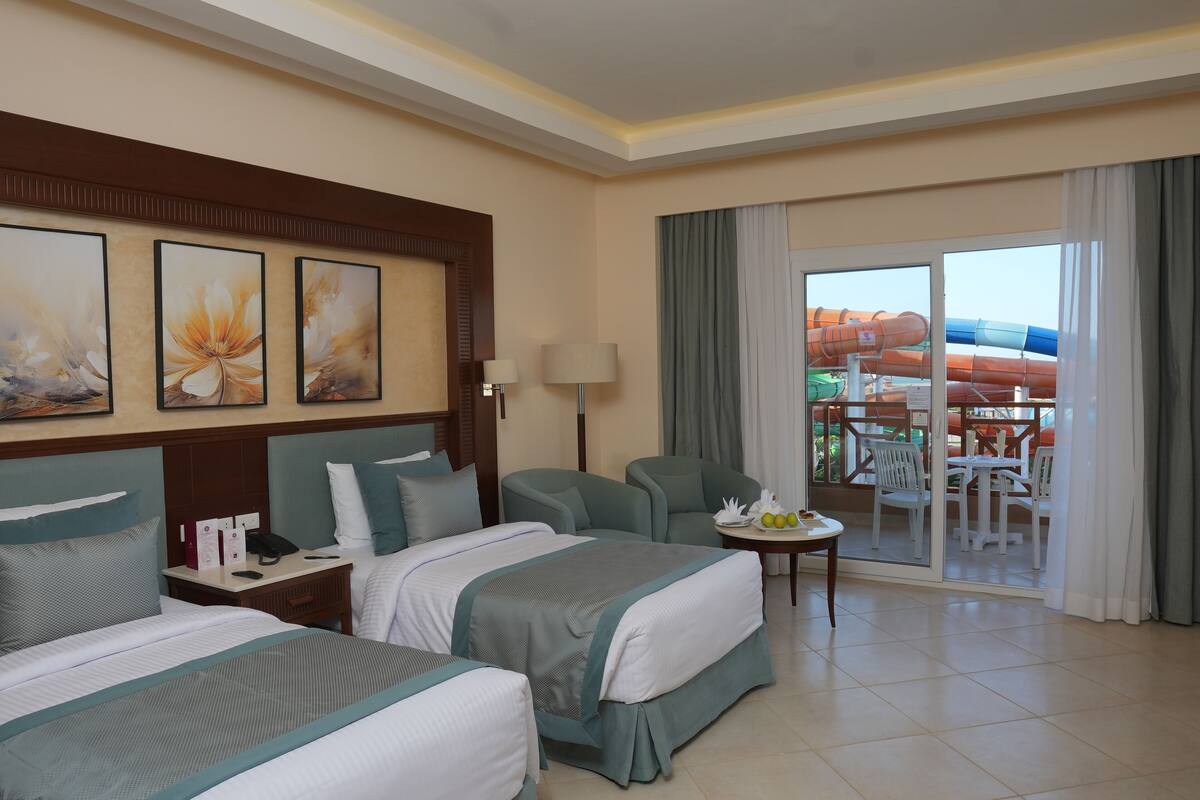 A hotel room with two beds, a desk, a chair, and a balcony with a water slide.