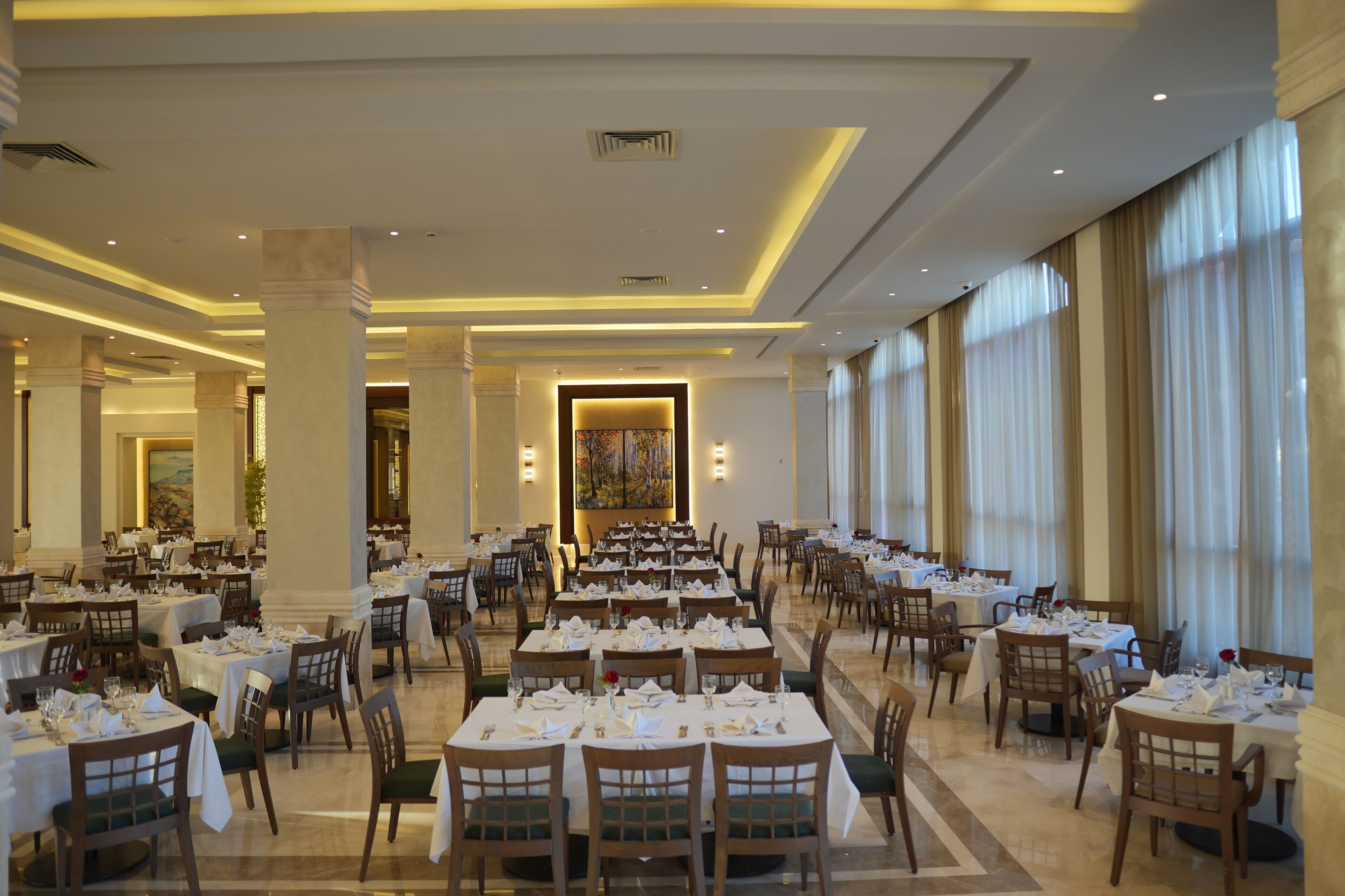 A spacious dining area with multiple tables and chairs, large windows, and a central art piece.
