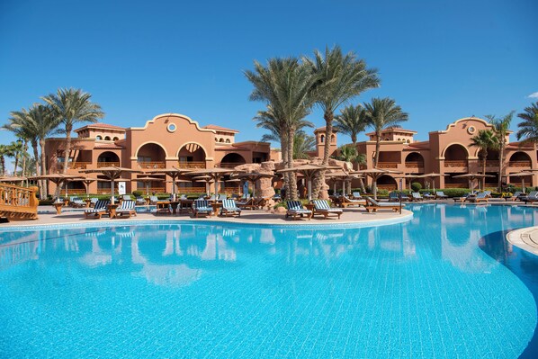 Un resort con piscina, palmeras y un edificio con arcos.