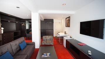 Una habitación de hotel moderna con un sofá gris, una mesita, un televisor, un escritorio y un armario.