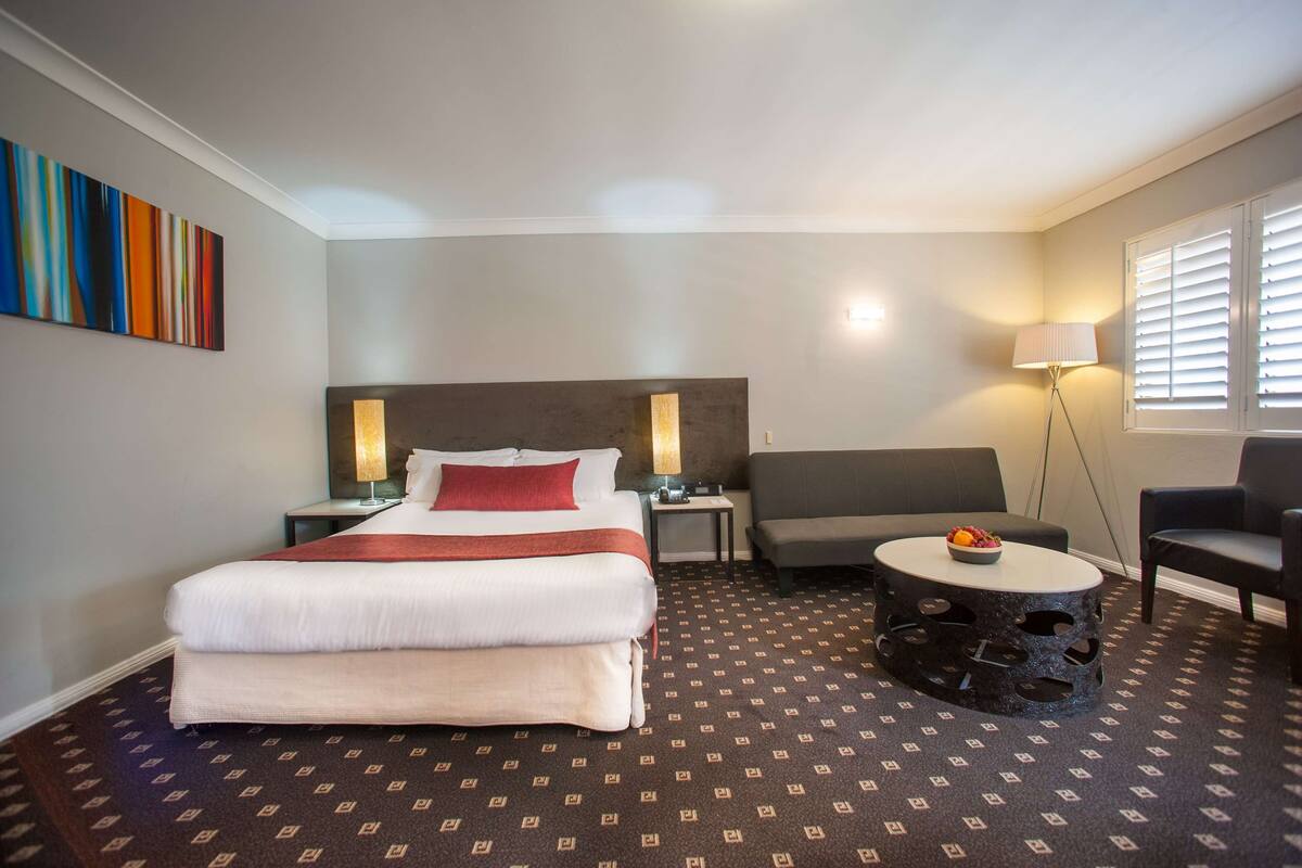 A hotel room with a bed, a sofa, a small table with fruit, and a lamp.