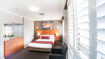 A hotel room with a bed, bedside tables, a desk, a chair, a mirror, and a painting on the wall.