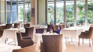 A restaurant with multiple tables and chairs, large windows, and a view of greenery outside. - Ramada Hotel & Suites Sydney Cabramatta (Cabramatta)