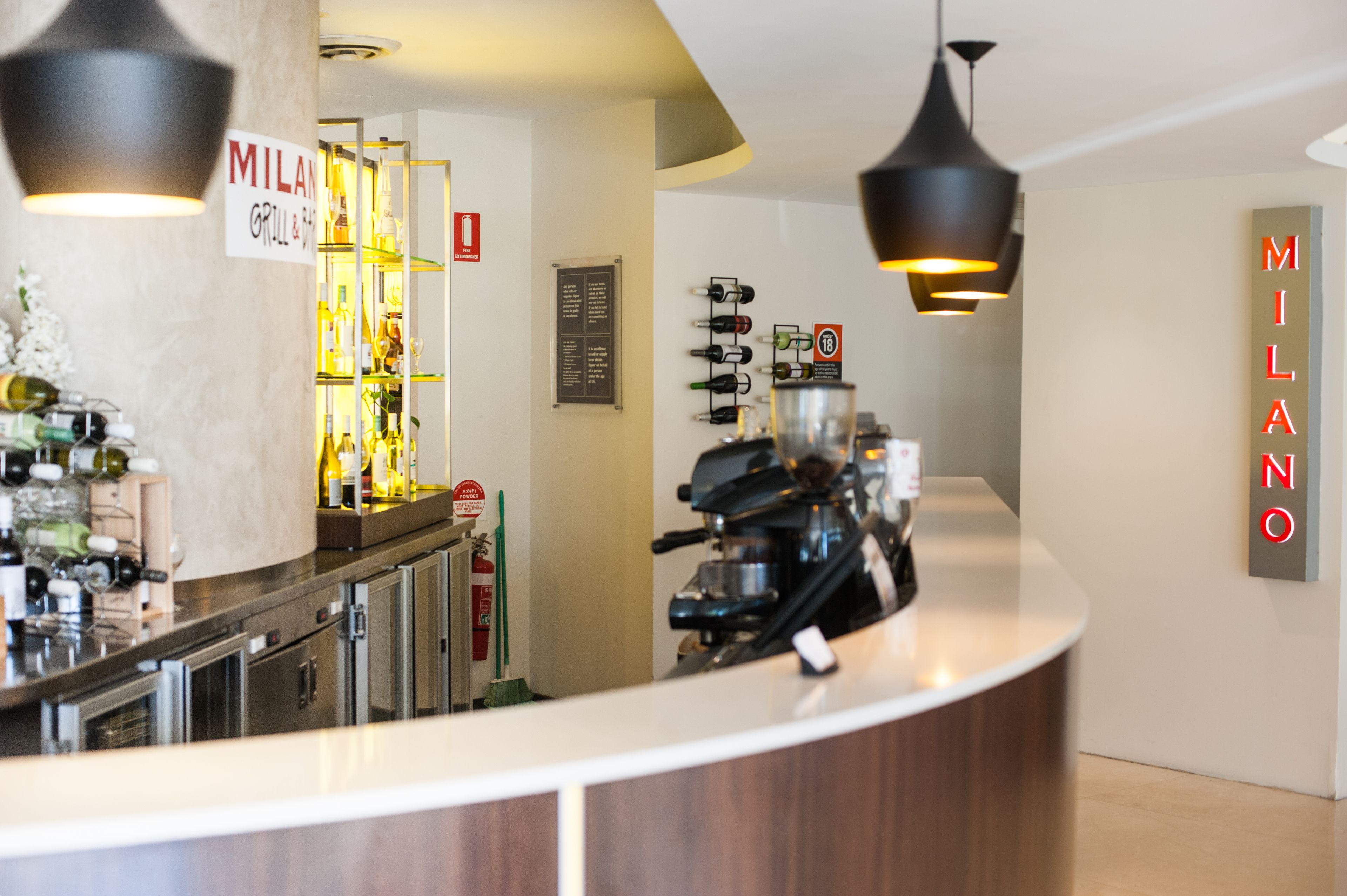 Zona de bar moderna amb un mostrador, ampolles de vi i una màquina de cafè.