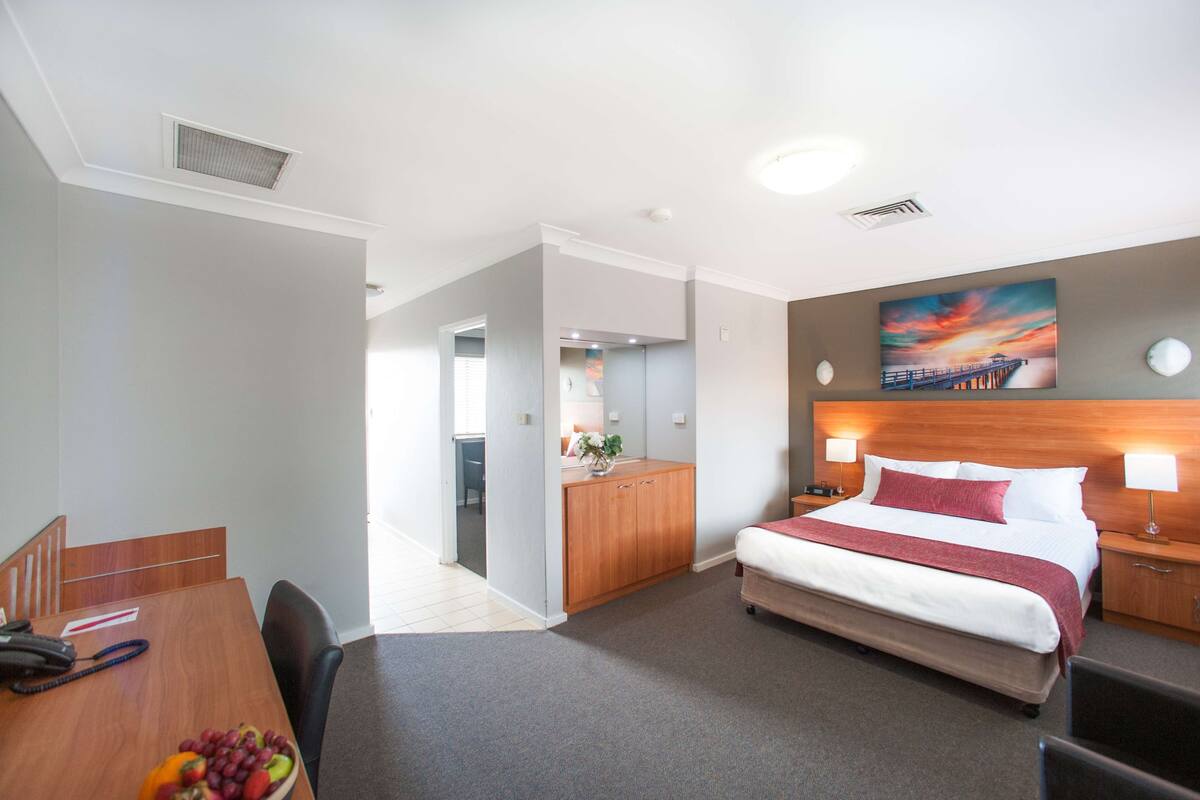 A hotel room with a large bed, a desk with a telephone, and a dining area with a table and chairs.