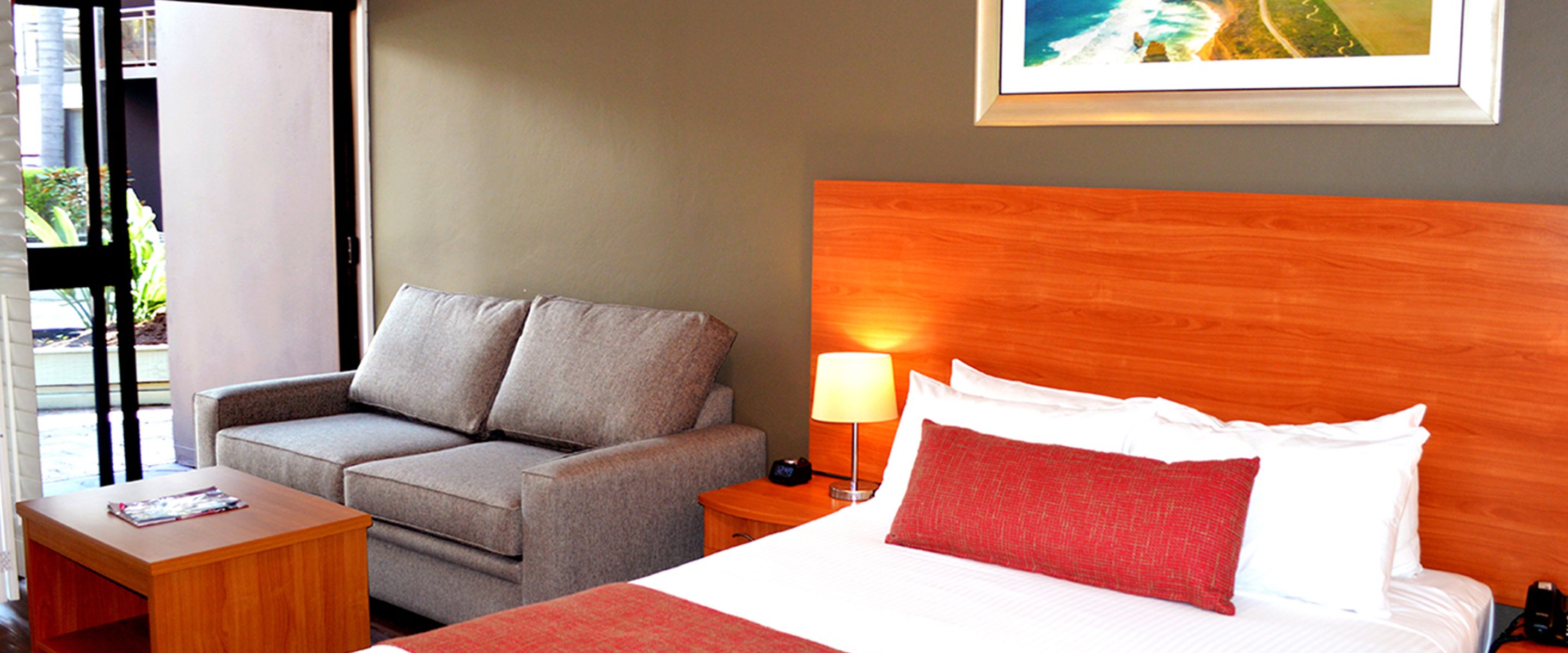 A hotel room with a bed, a sofa, a nightstand, and a small table.