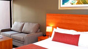A hotel room with a bed, a sofa, a nightstand, and a small table.