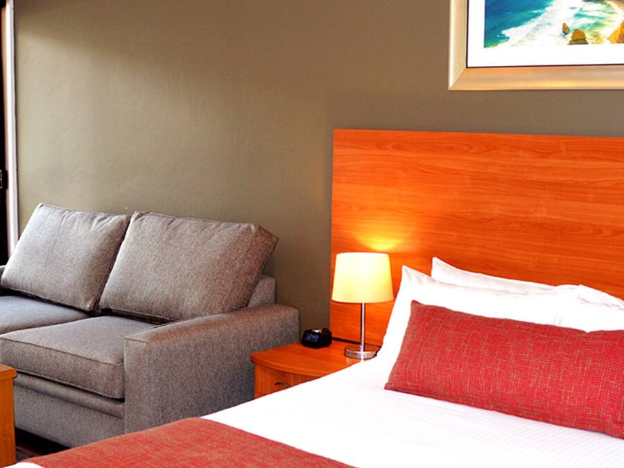 A hotel room with a bed, a sofa, a nightstand, and a small table.