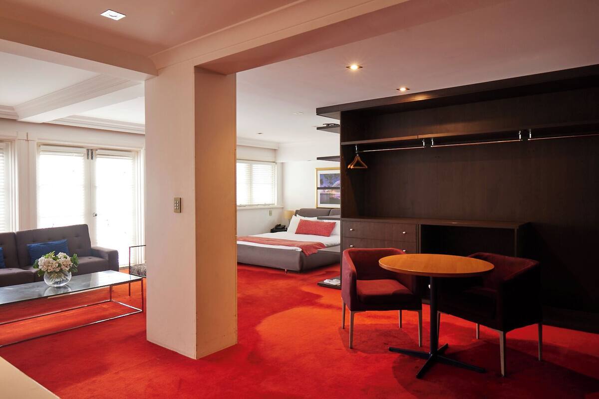 A modern hotel room with a red carpet, a sofa, a bed, and a small table with a vase of flowers.