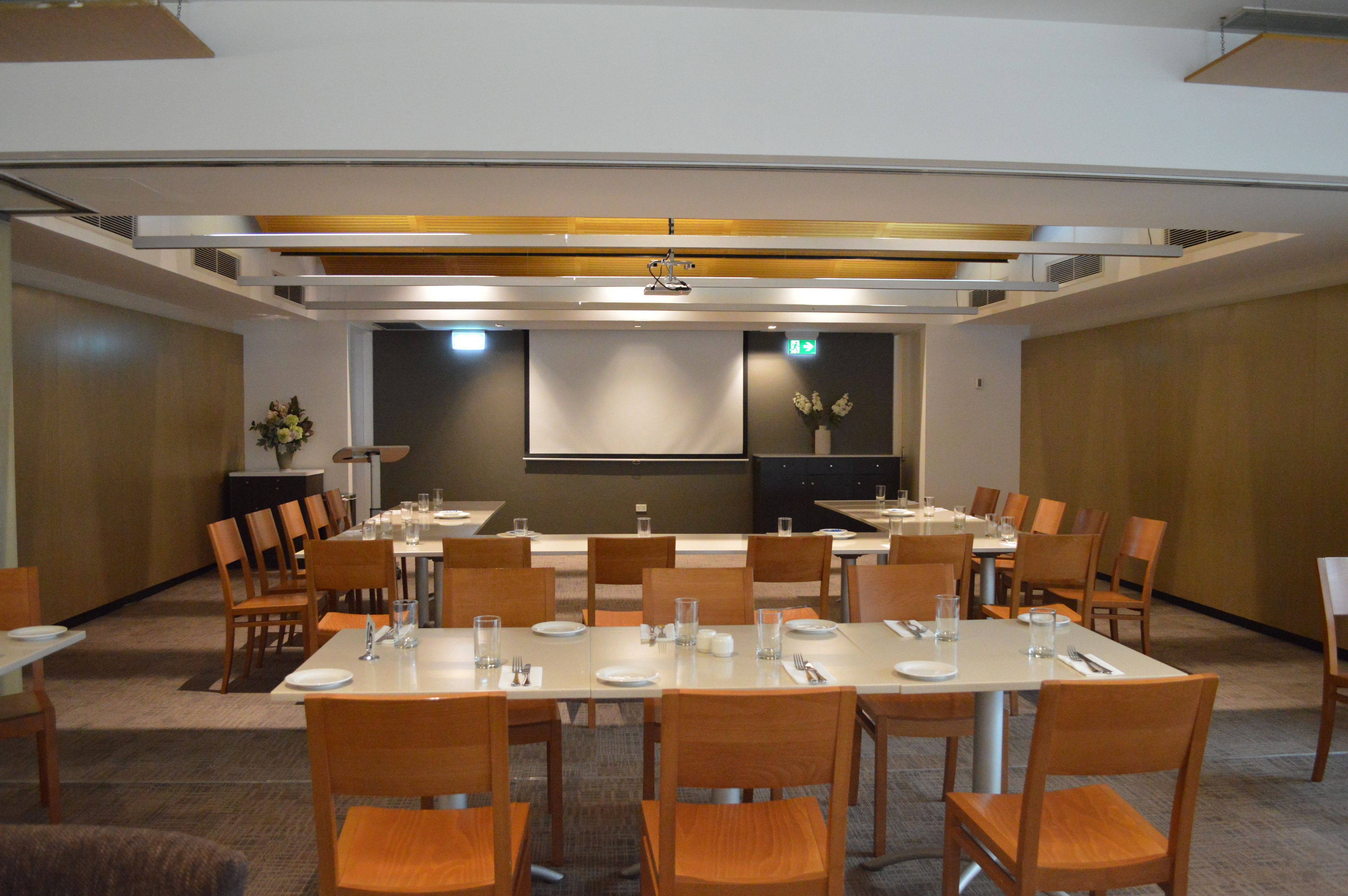 Une salle de conférence dotée de plusieurs tables et de chaises, et équipée de plaques nominatives, de verres à eau et d’un écran de projection.