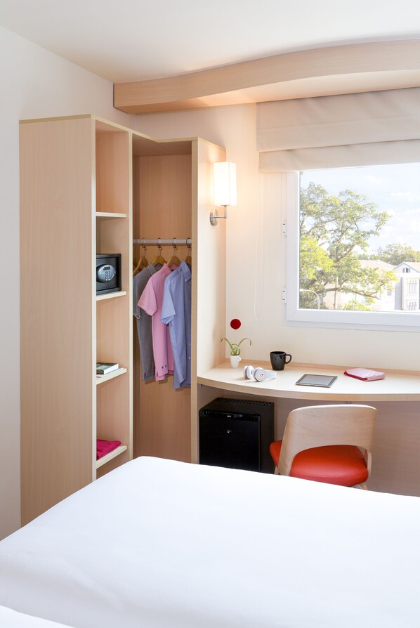 Une chambre d’hôtel comprenant un lit, un bureau avec une chaise, une armoire, une fenêtre avec vue et une petite table sur laquelle se trouvent un vase et une tasse.