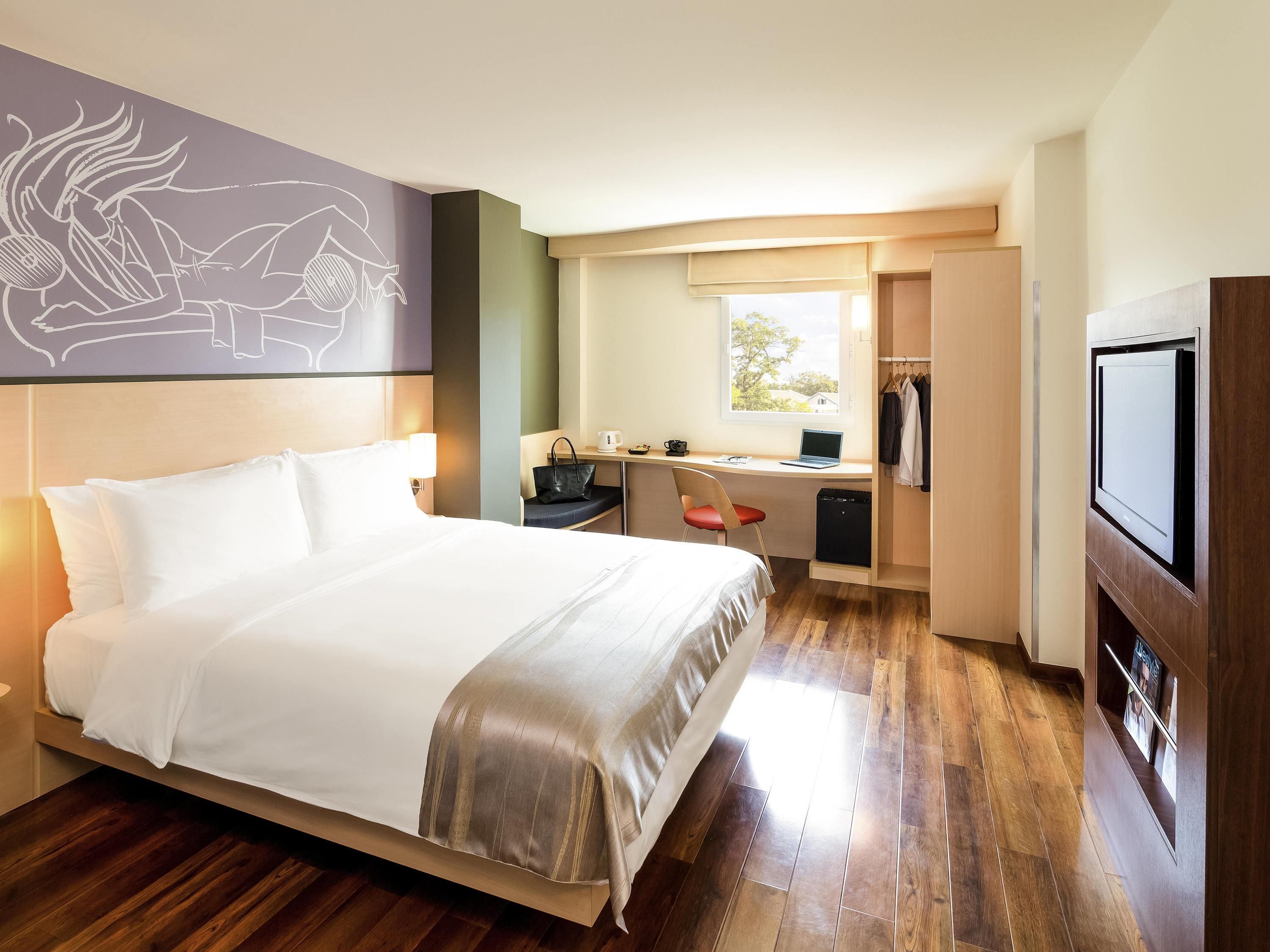 A hotel room with a bed, desk, chair, and TV.