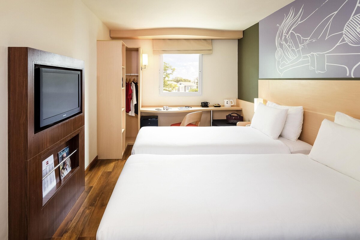 Une chambre d’hôtel avec deux lits, un bureau, une télévision et un placard.