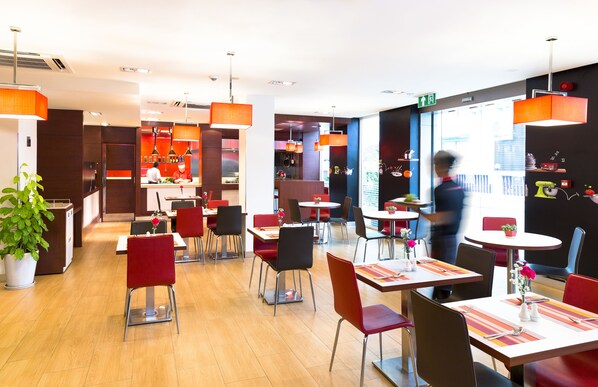 Un restaurante moderno con sillas rojas y negras, mesas de madera y lámparas colgantes naranjas.